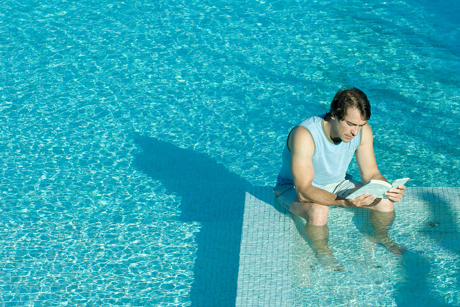 Man sitting in swimming pool, reading Photograph by PhotoAlto/Odilon Dimier