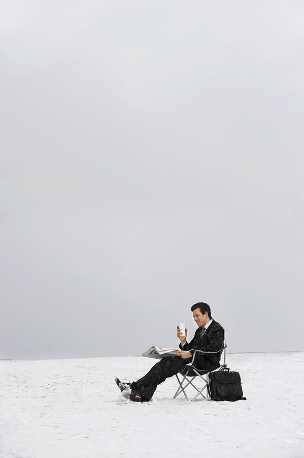 Man Sitting on a Chair Outdoors in Snow and Reading a Newspaper Photograph by John Cumming
