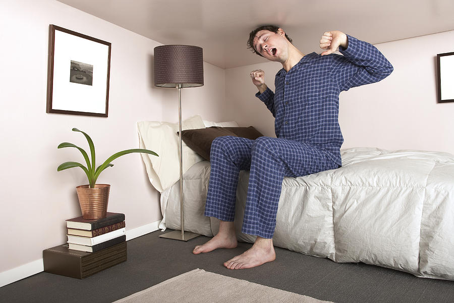 Man sitting on bed stretching in miniature bedroom Photograph by Troy Aossey