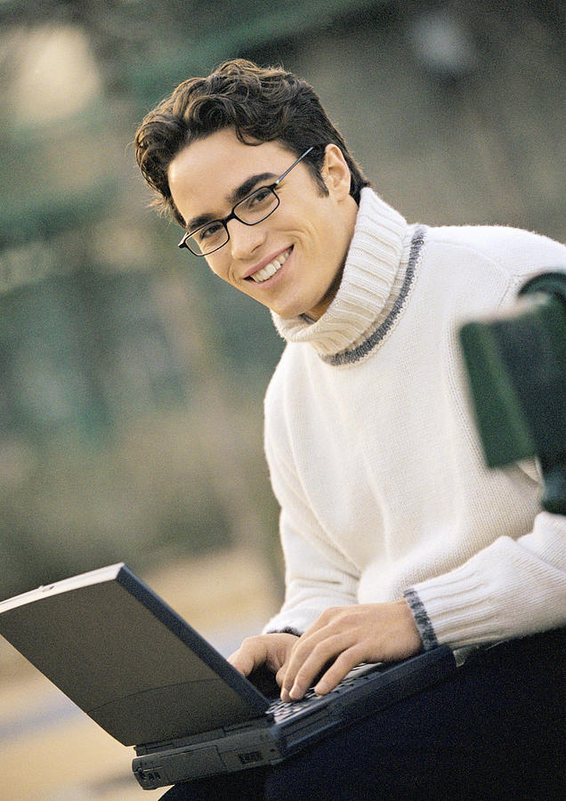Man sitting on bench with laptop computer, portrait Photograph by Eric Audras