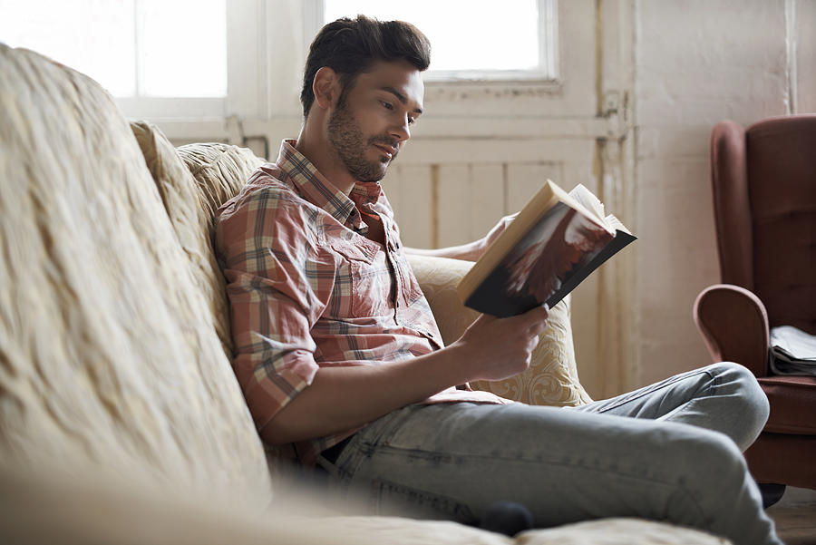 Man sitting on sofa reading a book Photograph by Morsa Images