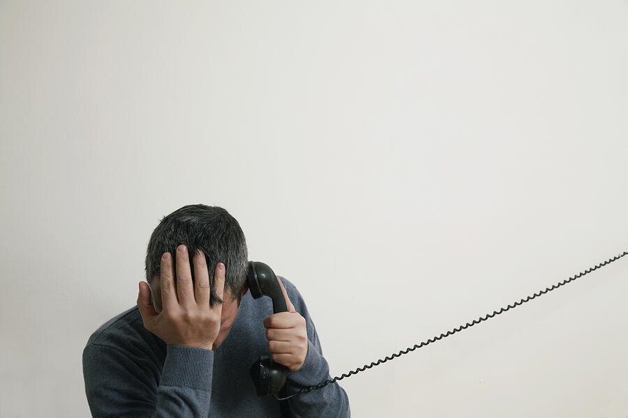 Man sitting on stairs using telephone, hand to head Photograph by Push