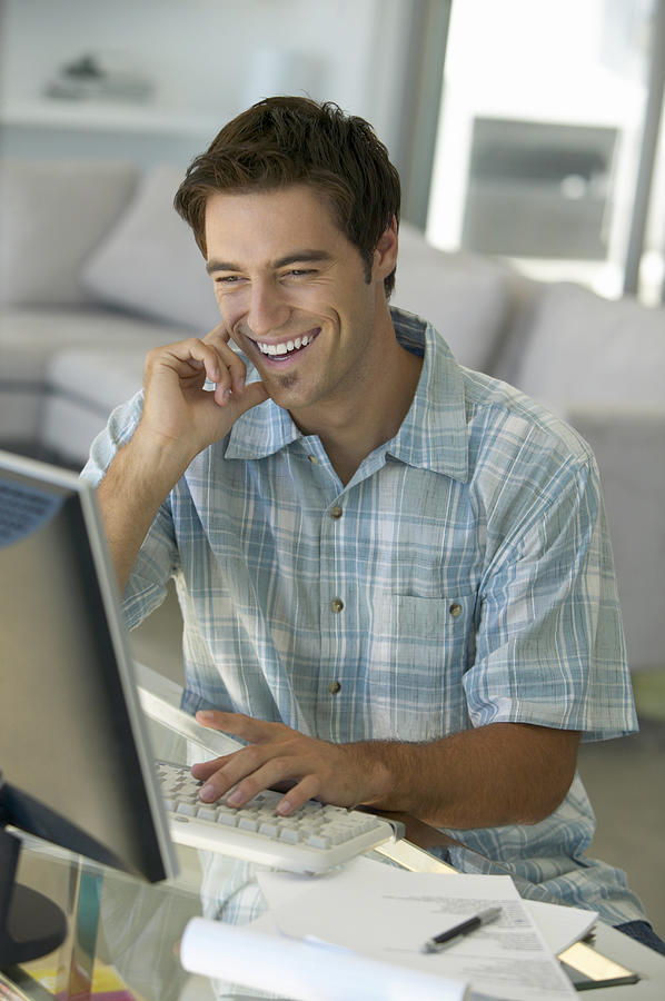 Man Smiling Sitting at a Desk in a Living Room Using a Computer Photograph by Flying Colours Ltd