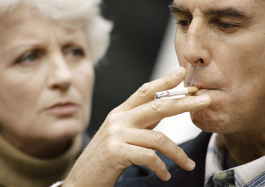 Man smoking, woman blurred in background, close-up. Photograph by Eric Audras