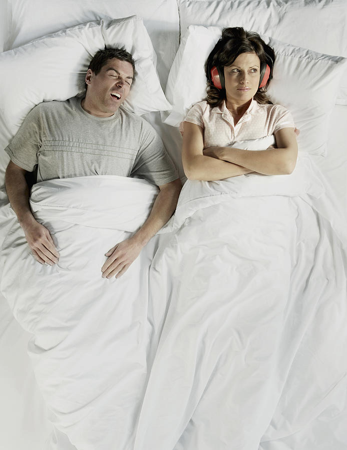 Man snoring in bed with woman wearing ear defender Photograph by Flashpop