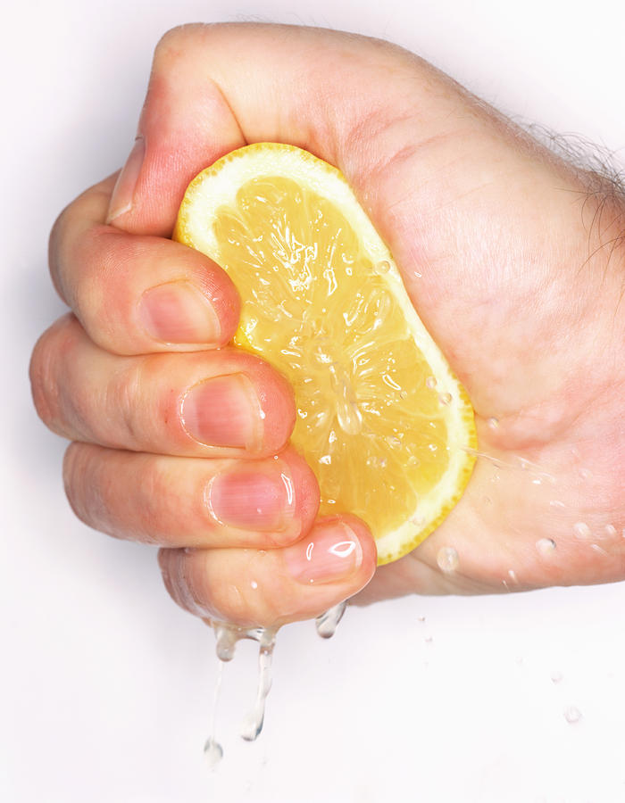 Man squeezing cut lemon in fist, close-up Photograph by Peter Dazeley