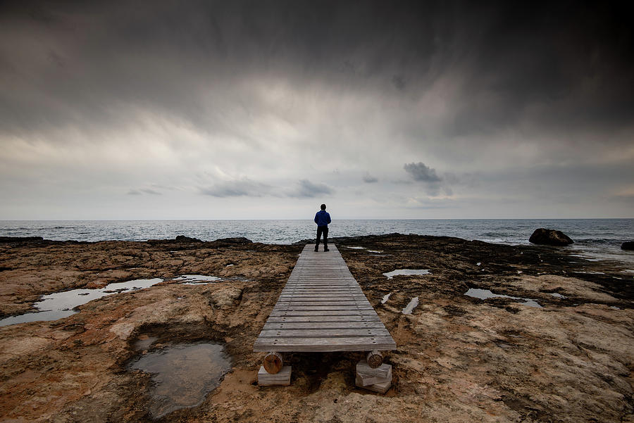 Man standing alone at the edge of rocky beach in Stormy Weather Photograph by Michalakis Ppalis