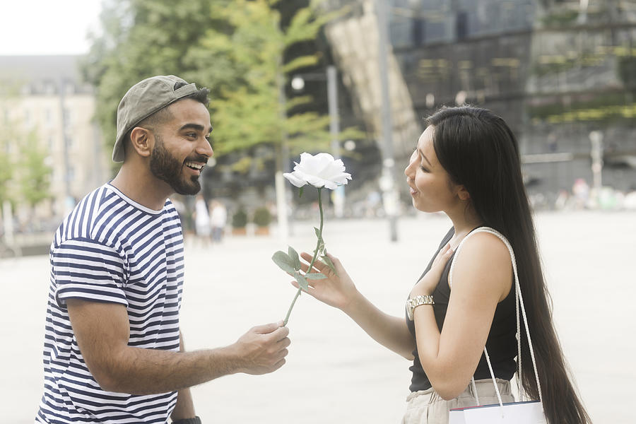 Man standing in city square giving his girlfriend a white rose Photograph by Sigridgombert