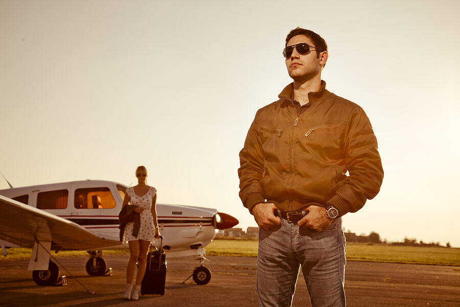 Man standing in front of propeller airplane, woman in background Photograph by Lumi Images/Hudolin-Kurtagic