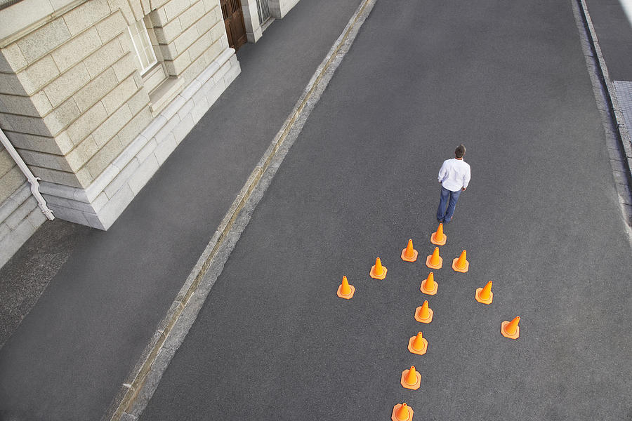 Man standing in front of traffic cones in arrow-shape Photograph by Martin Barraud
