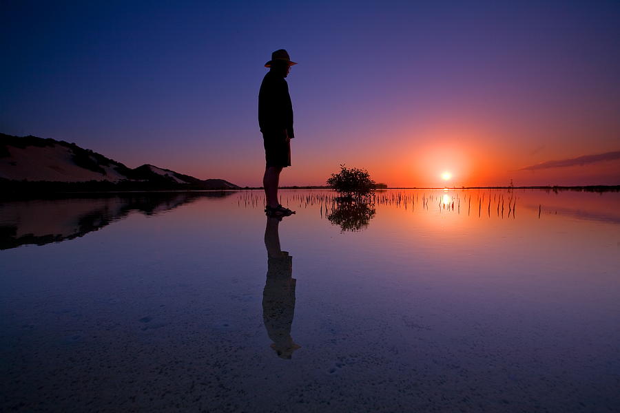 Man standing in river at sunset Photograph by Visionandimagination.com
