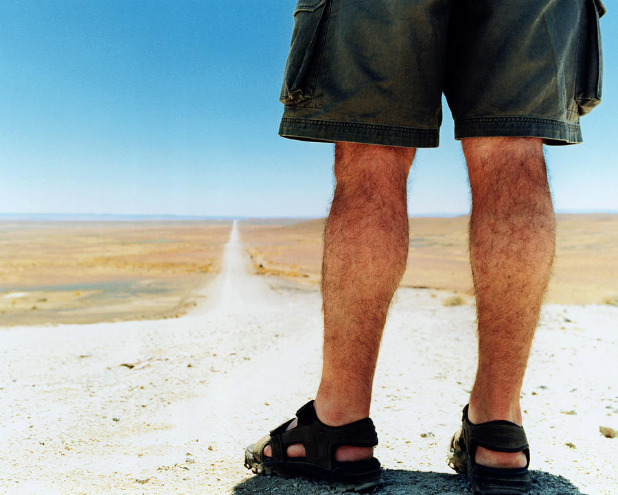Man standing on country road, rear view (low-section) Photograph by Clarissa Leahy