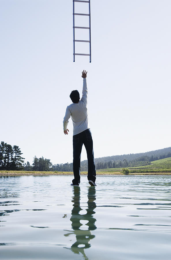 Man standing on water reaching for ladder rear view Photograph by OJO Images