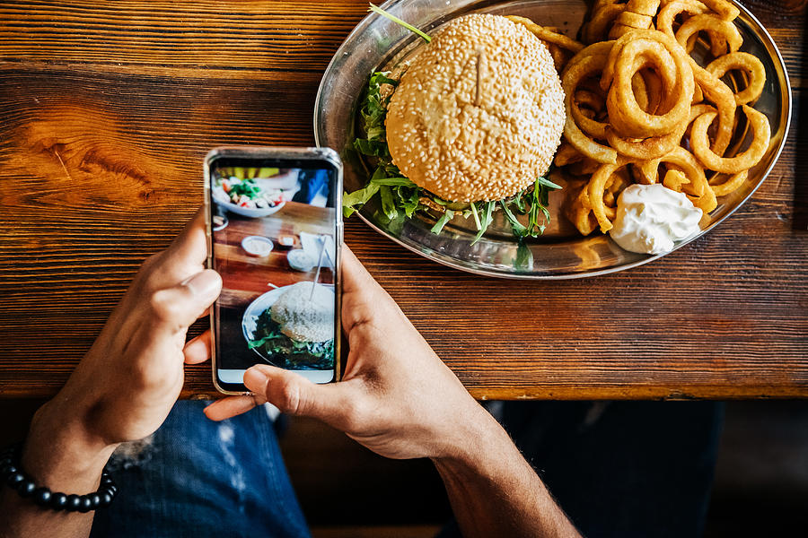 Man Talking Picture Of Burger With Smartphone Photograph by Hinterhaus Productions