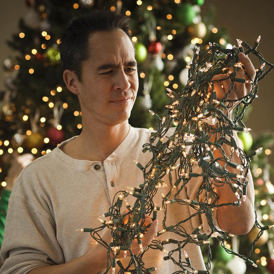 Man Untangling Christmas Tree Lights Photograph by RubberBall Productions