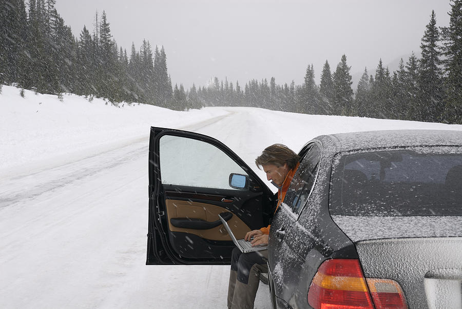 Man using computer to contact help in snowstorm Photograph by AscentXmedia