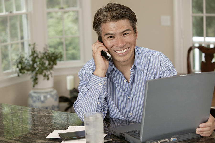 Man using laptop and talking on cell phone Photograph by Comstock Images