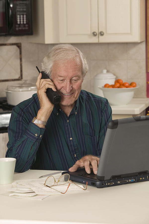 Man using laptop and talking on telephone Photograph by Comstock Images