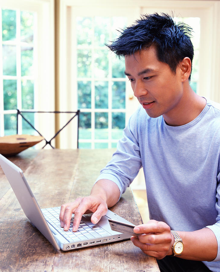 Man using laptop at home, holding credit card Photograph by Noel Hendrickson