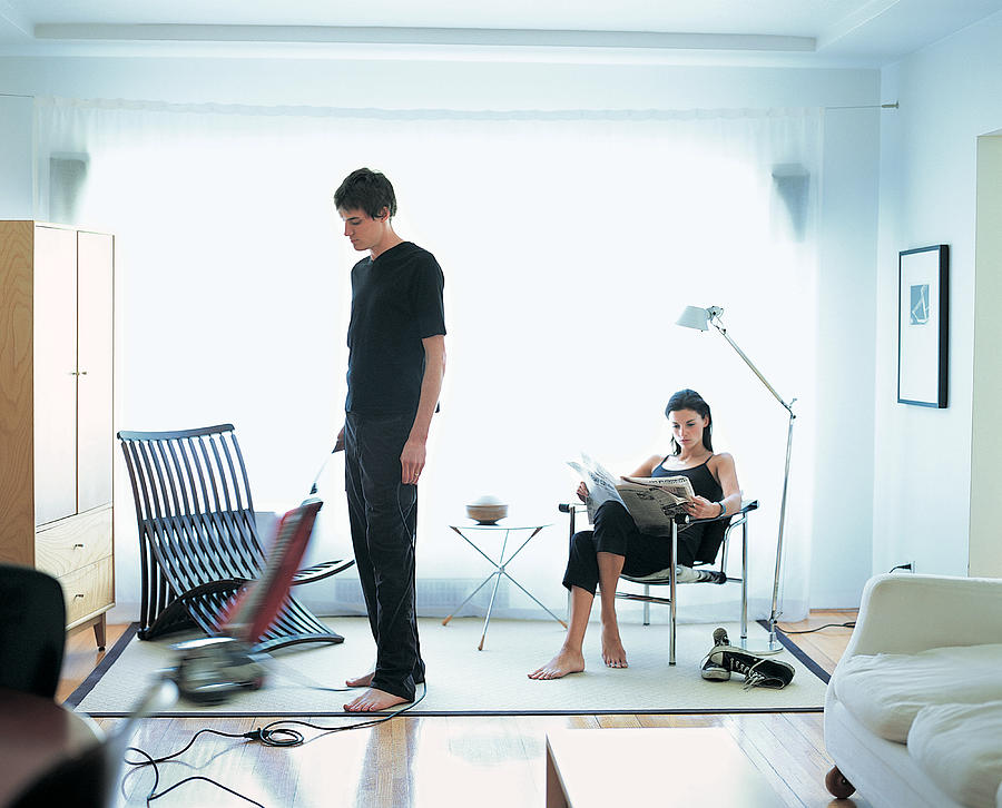 Man Vacuuming, While Woman Reads Newspaper Photograph by Digital Vision.