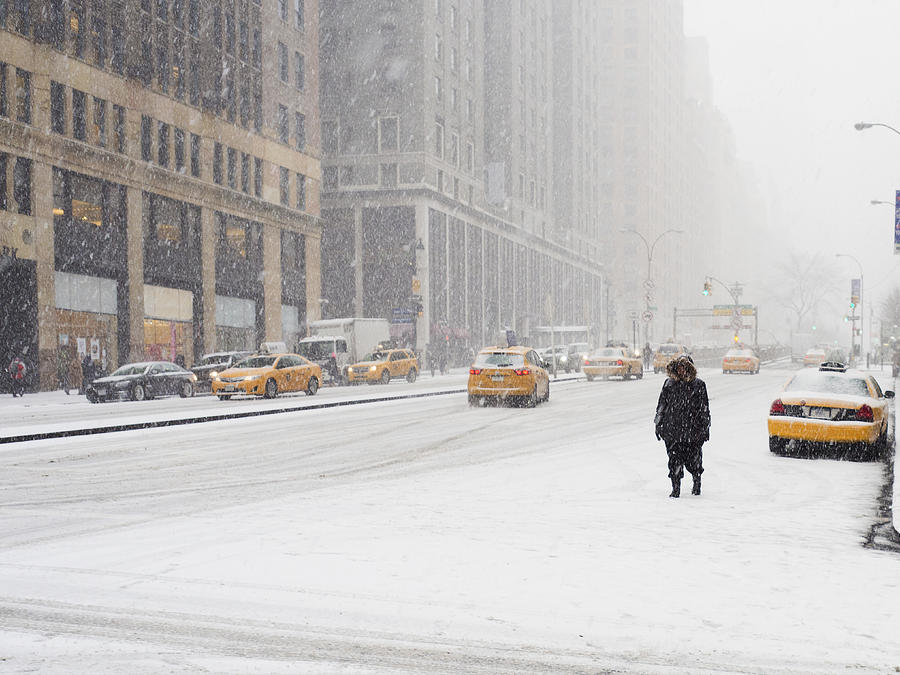 Man walking in a city in the snow during a blizzard, yellow taxis on the street. Photograph by Mint Images