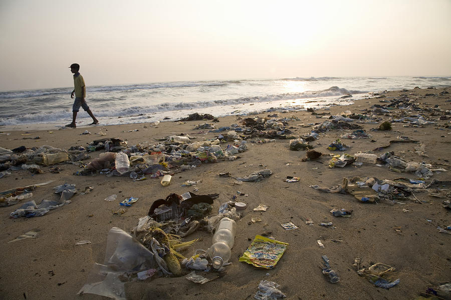 Man walking on a beach full of garbage Photograph by John Lund