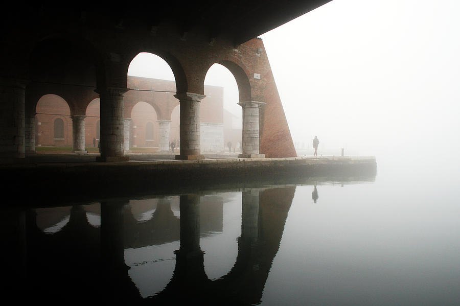 Man walking under arches in historic building in Venice in a foggy day Photograph by © Nico Piotto