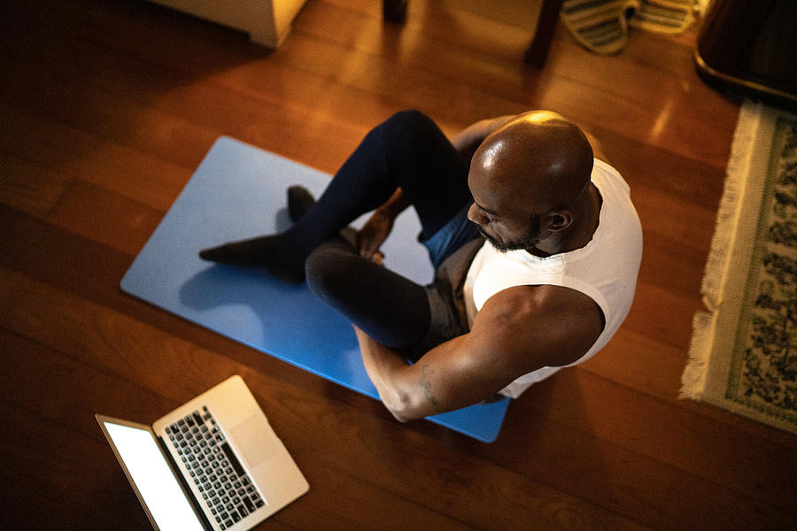 Man watching gym class on laptop and doing exercises at home Photograph by FG Trade