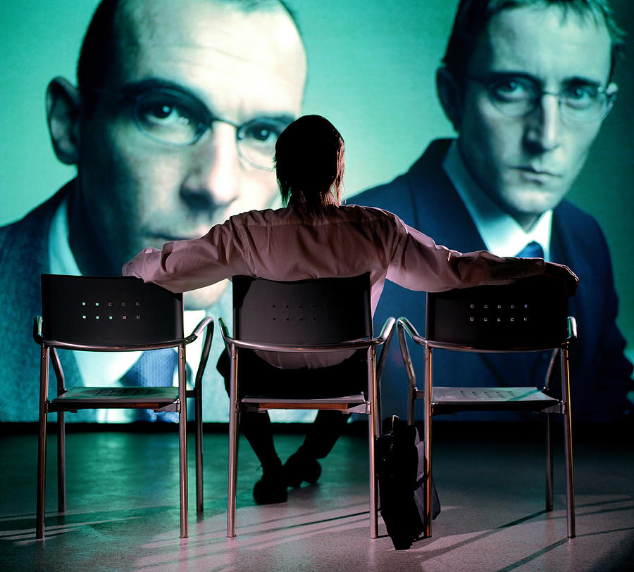 Man watching projection of two businessmen, rear view Photograph by Colin Hawkins