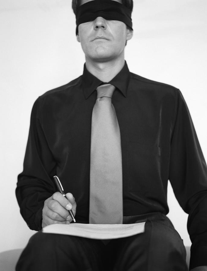 Man wearing blindfold, writing in a book, b&w. Photograph by Matthieu Spohn