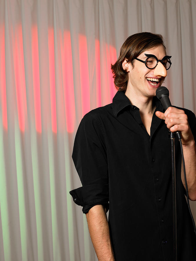 Man wearing joke nose and glasses, holding microphone, smiling Photograph by John Rowley