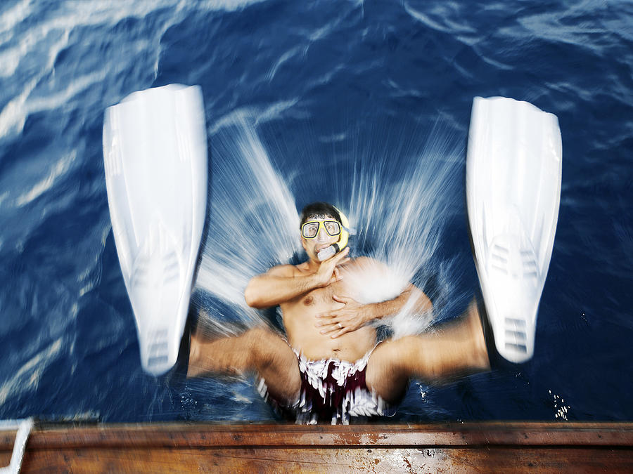 Man wearing snorkel and fins, falling from boat into water, portrait Photograph by David Trood