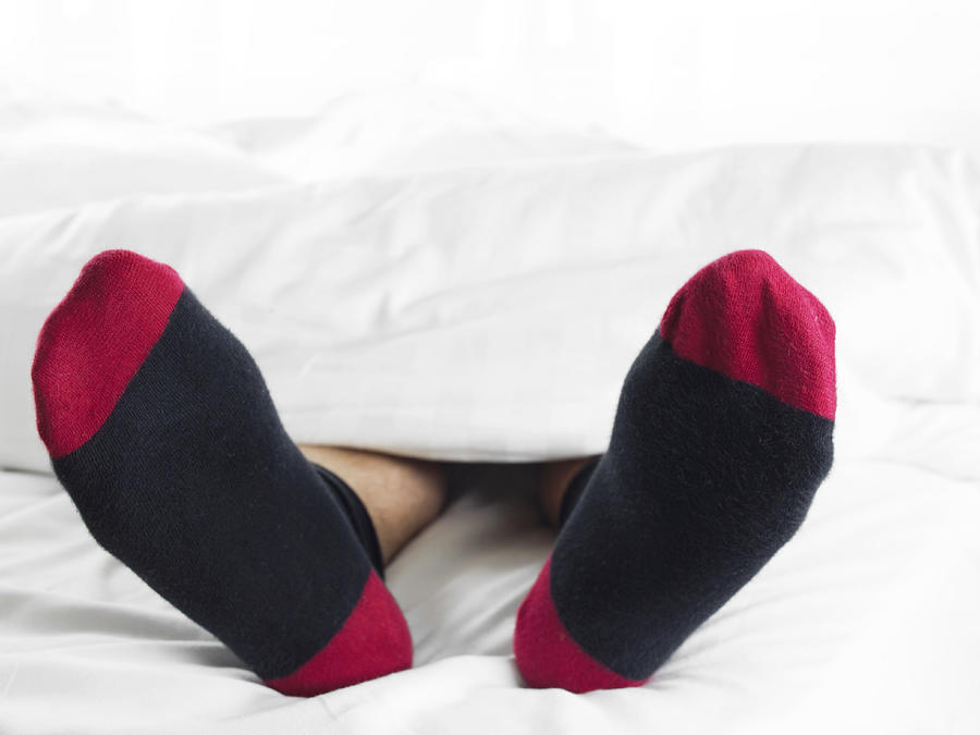 Man Wearing Socks Underneath a Duvet in Bed Photograph by Digital Vision.