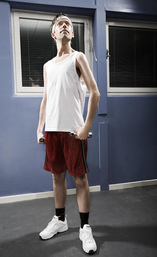 Man wearing sweatband standing in gym holding weights, low angle view Photograph by Holloway