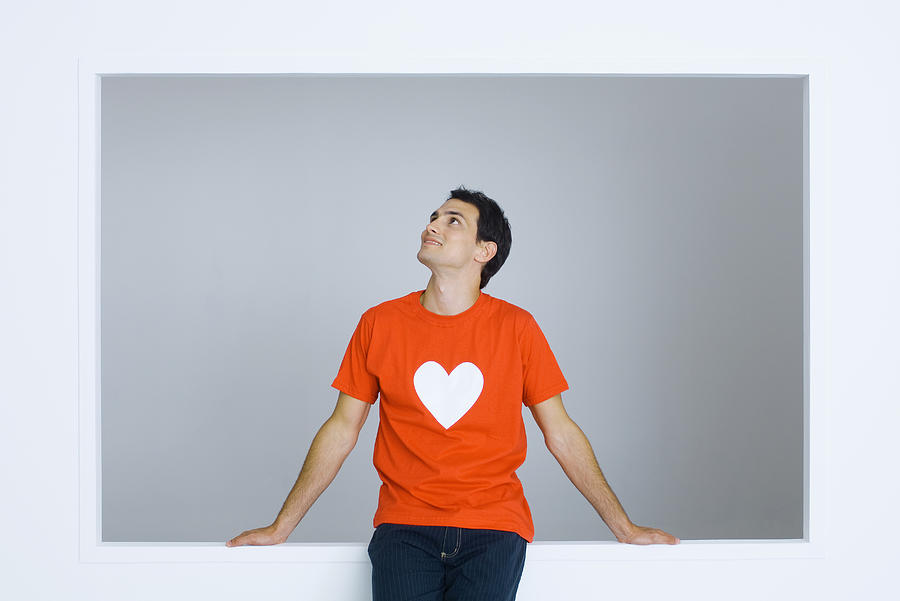 Man wearing tee-shirt with heart symbol, looking up, smiling Photograph by PhotoAlto/Michele Constantini
