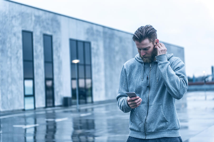 Man with beard listens to music on smart phone outside Photograph by Mikkelwilliam
