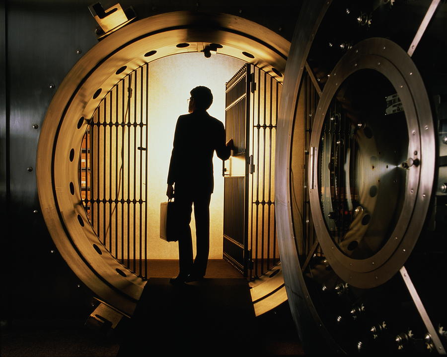 Man with briefcase silhouetted in open door of bank vault Photograph by Andy Sacks