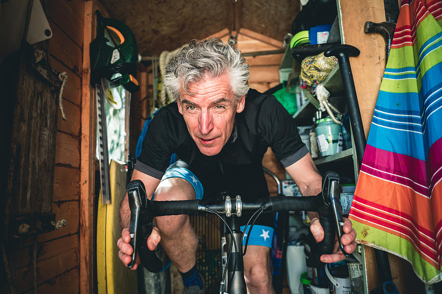 Man with determined expression exercising on a static bike in the shed Photograph by Lambert And Young