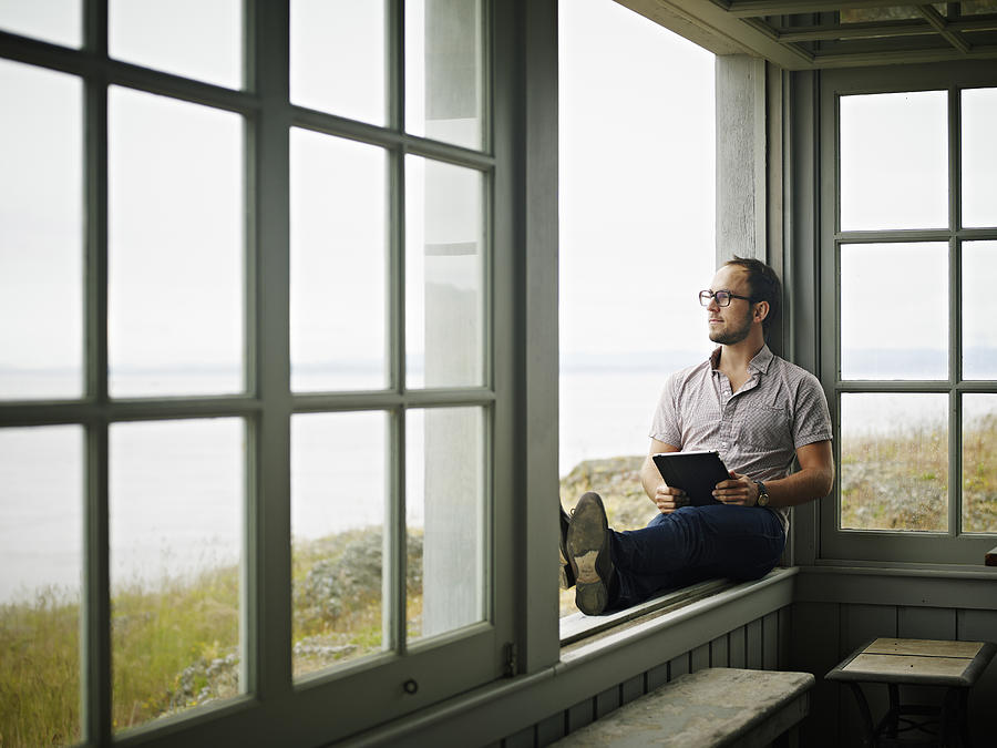 Man with digital tablet sitting on window ledge Photograph by Thomas Barwick