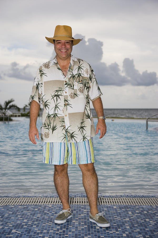 Man with hat and tropical shirt by pool, smiling portrait Photograph by Juan Silva