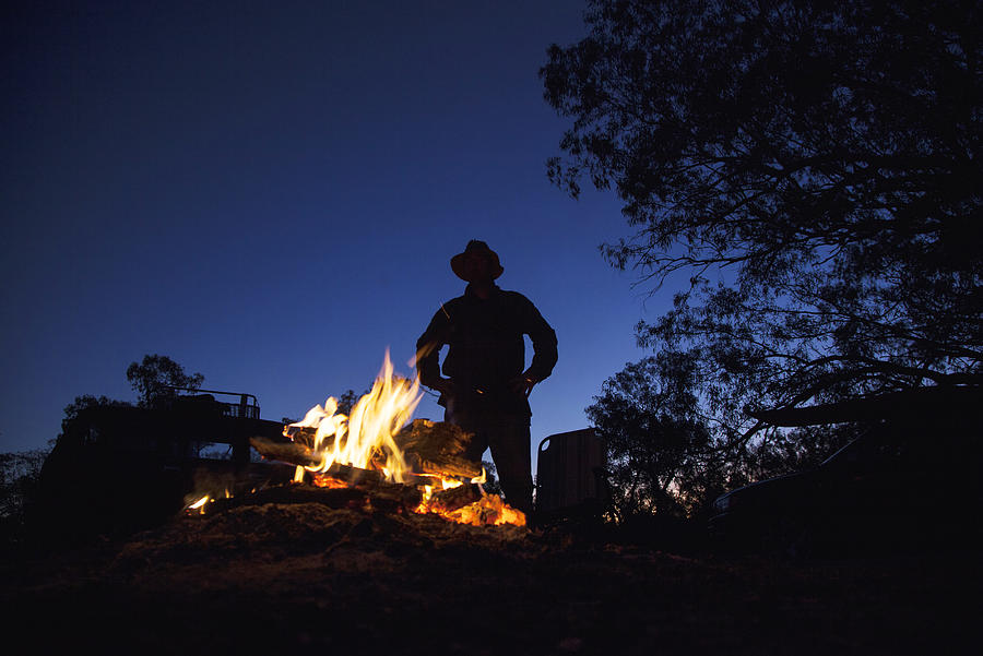 Man with hat standing by campfire. Photograph by David Trood