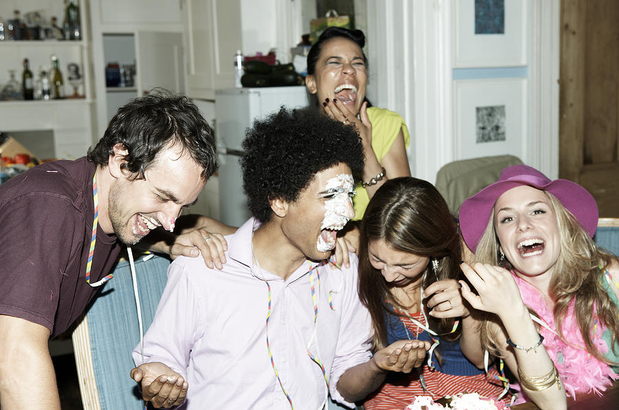 Man with icing on his face laughing with friends Photograph by John Howard