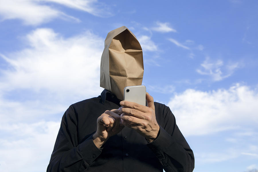 Man with paper bag above his head using cell phone Photograph by Westend61