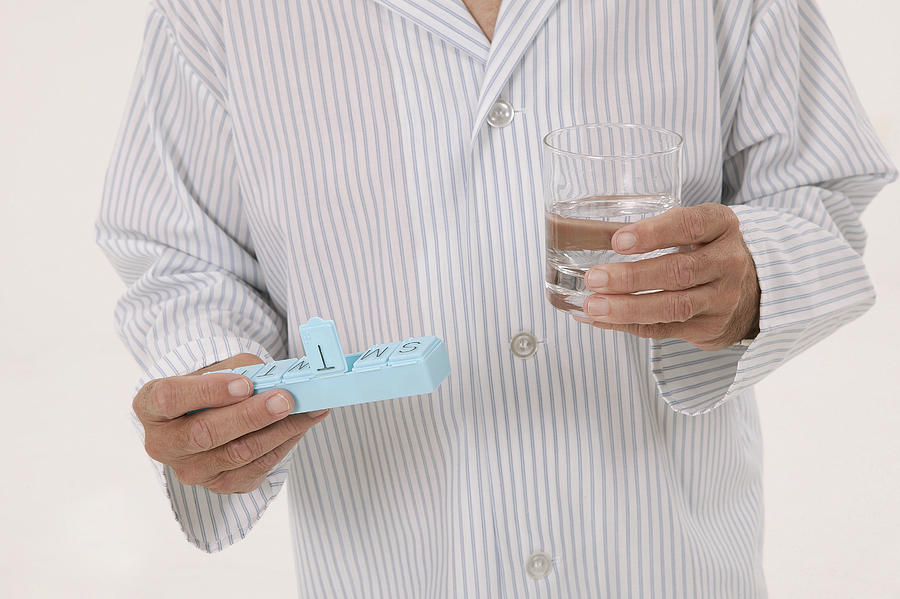Man with pill box and glass of water Photograph by Comstock Images