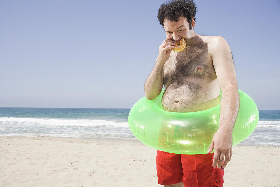 Man with pot belly eating a hamburger on the beach Photograph by Sian Kennedy