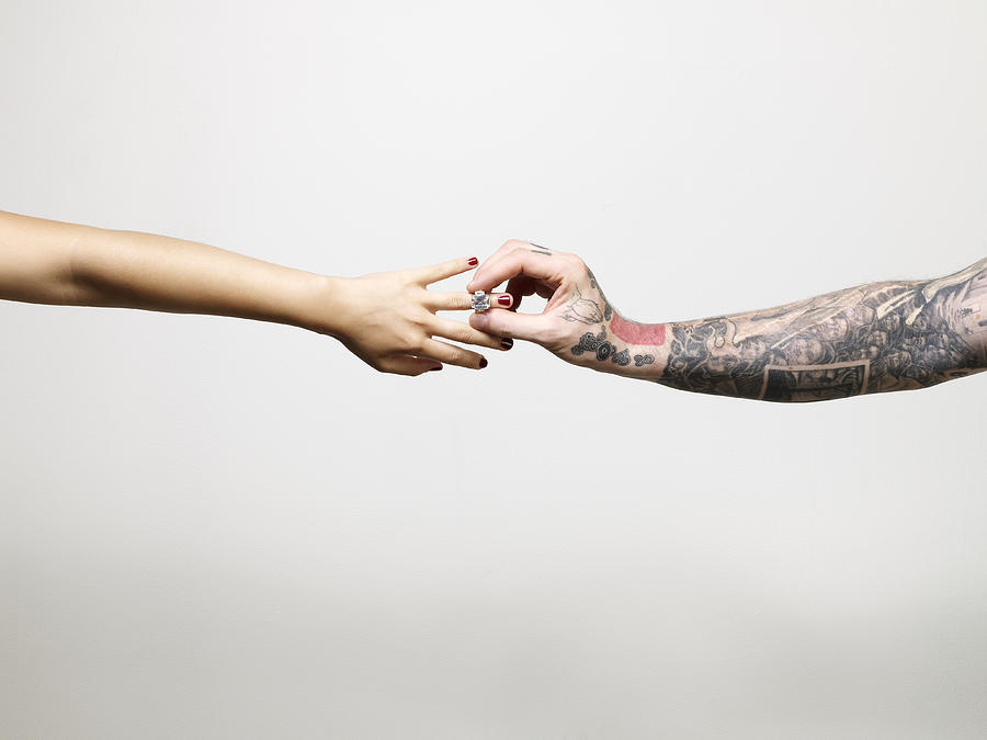 Man with tattooed arm placing ring on finger of young woman, close-up of arms and hands Photograph by Ballyscanlon