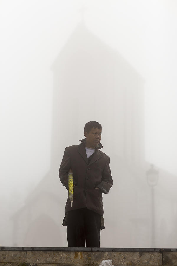 Man with umbrella at misty church Photograph by Merten Snijders