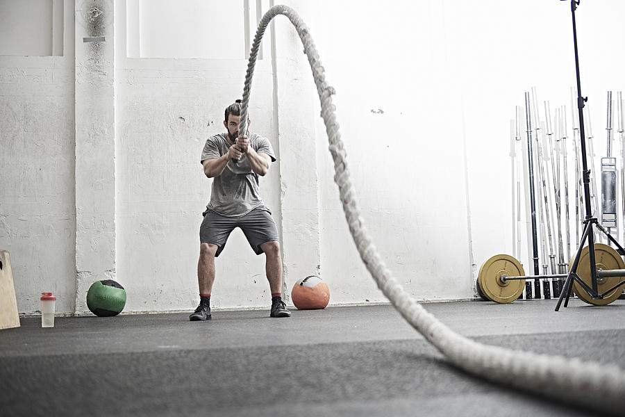 Man working out with battle rope in cross training gym Photograph by Jakob Helbig