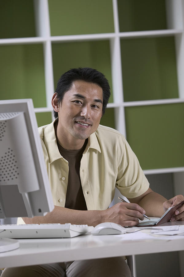 Man writing check by computer Photograph by Comstock Images