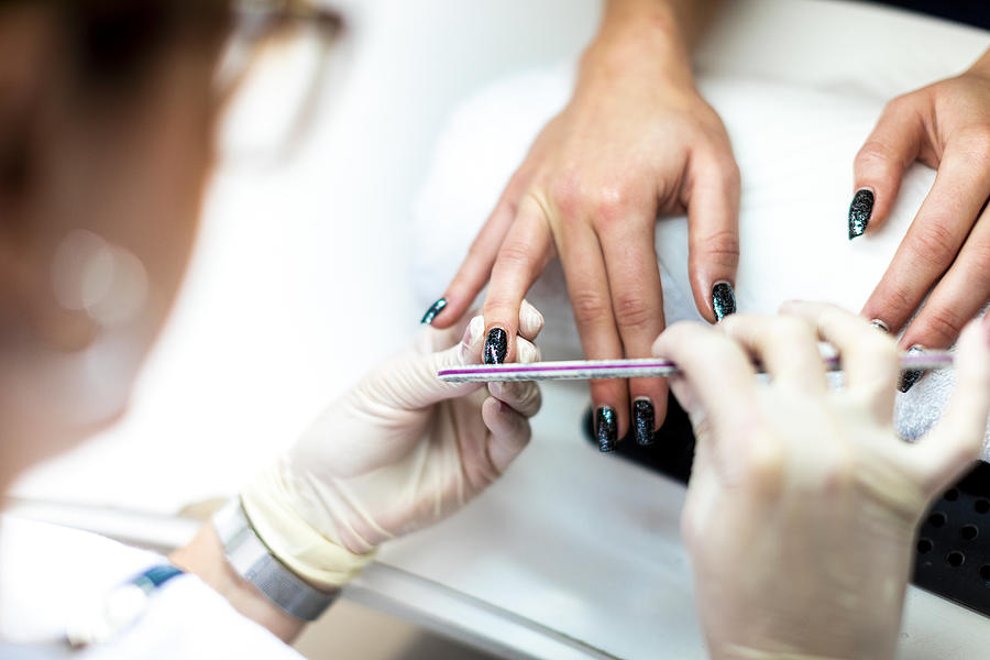 Manicurist using a file on a fingernail to remove excess cuticles and prepare it for painting Photograph by Extreme-photographer